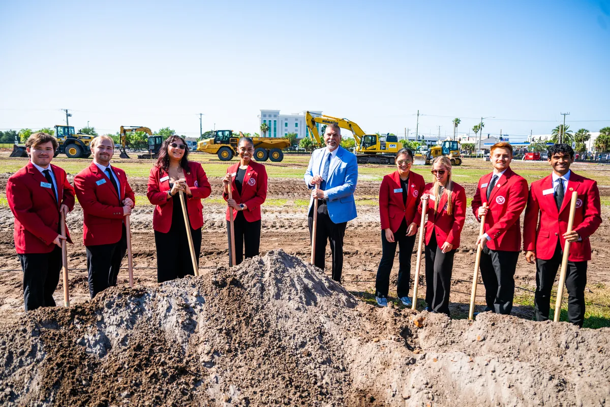 President Nicklow with several President's Ambassadors, posed behind a dirt mound with shovels.