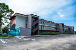 A three story apartment building with covered stairwells facing a parking lot. A large colorful mural covers one end of the building